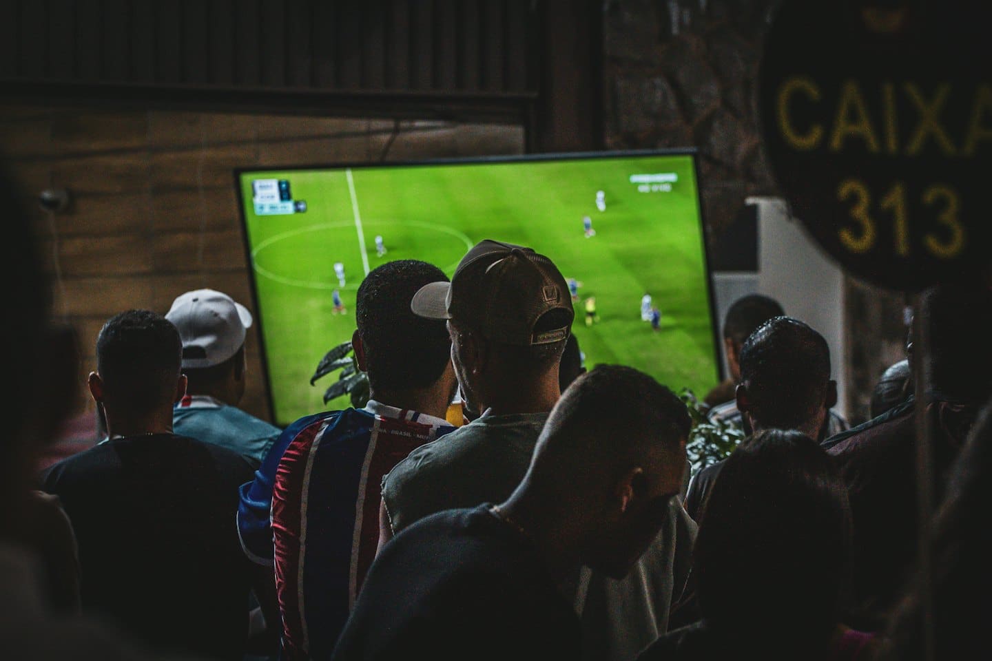 Persone guardano una partita di calcio su uno schermo TV luminoso.